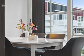 Een moderne eethoek met een witte tafel, zwarte stoelen en een vaas met bloemen.