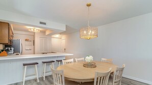 A modern kitchen with white cabinetry, a central island with stools, and a chandelier. - Steps to Beach! Spacious 3bd with pool! Murrells Inlet! Family friendly (Murrells Inlet)