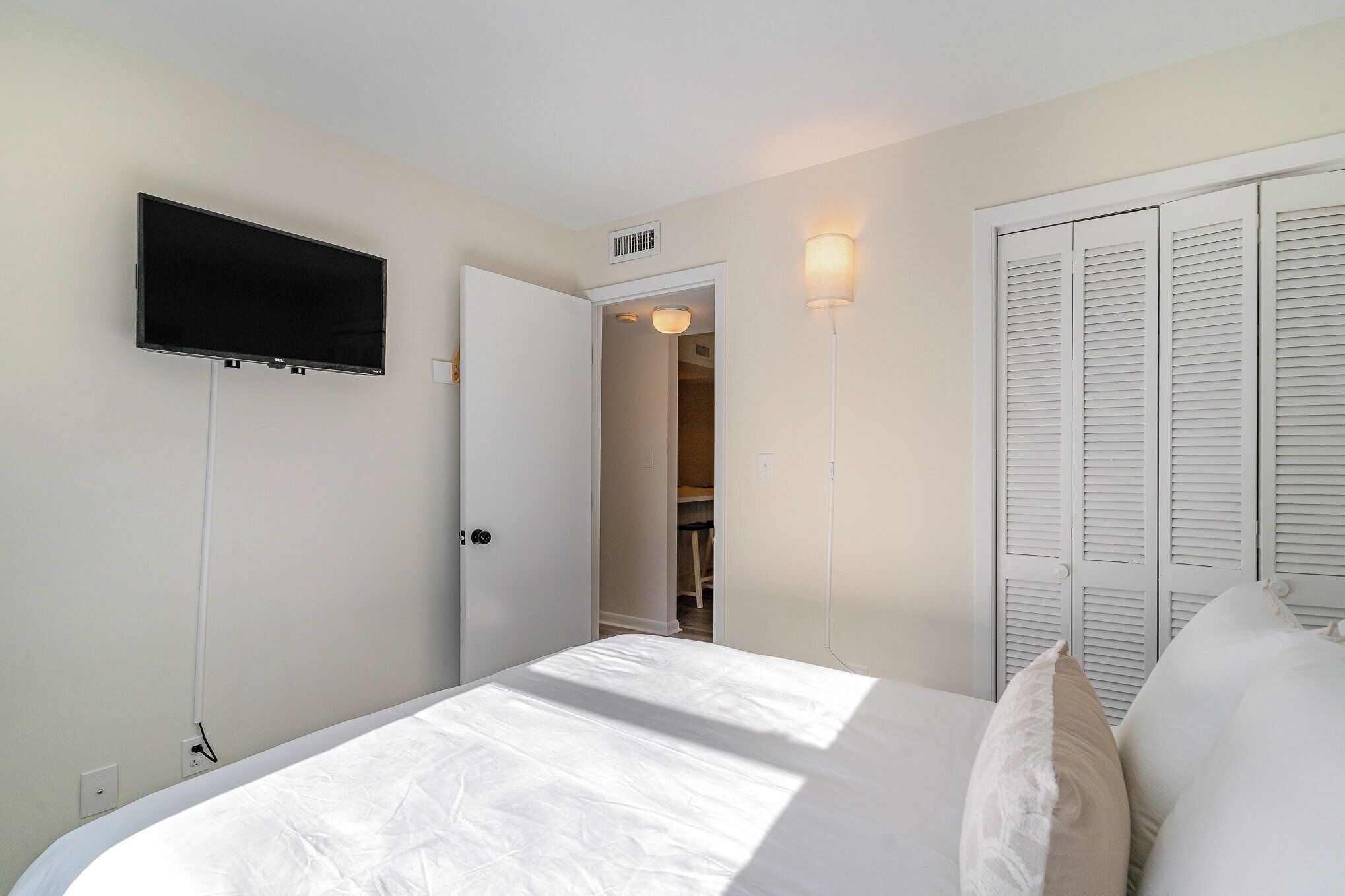 A bedroom with a bed, a TV mounted on the wall, and a closet with louvered doors.