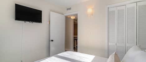 A bedroom with a bed, a TV mounted on the wall, and a closet with louvered doors.