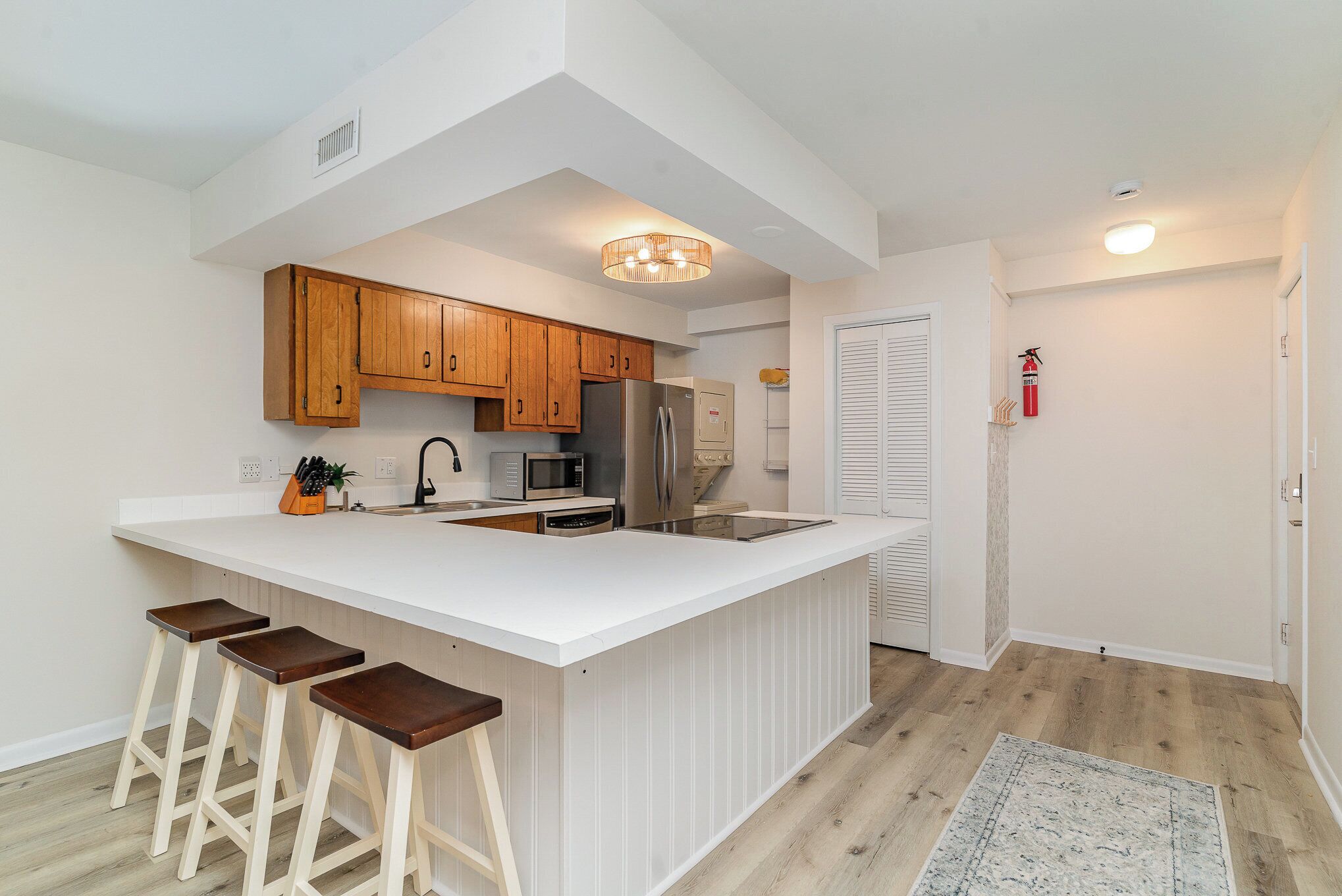 Une cuisine moderne avec des meubles en bois, un plan de travail blanc, un réfrigérateur en acier inoxydable et un îlot central intégré avec des tabourets de bar.