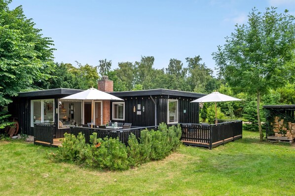Uma cabana preta com um deck, janelas amplas e uma chaminé.