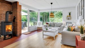 A modern living room with a fireplace, a sofa, a coffee table, and a view of the outdoors. - Cozy cottage near the beautiful Rågeleje beach. (Vejby)