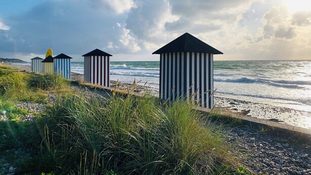 Beach huts with striped patterns and black roofs, positioned on a pebbled beach with grass in the foreground. - Cozy cottage near the beautiful Rågeleje beach. (Vejby)