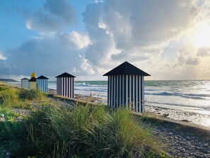 Beach huts with striped patterns and black roofs, positioned on a pebbled beach with grass in the foreground. - Cozy cottage near the beautiful Rågeleje beach. (Vejby)