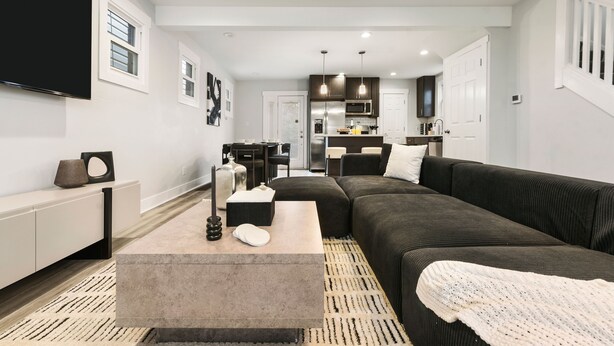 Un salon moderne avec un canapé foncé, une table basse beige et un téléviseur à écran plat fixé au mur.