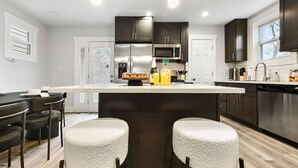 Une cuisine moderne avec des meubles de couleur sombre, des appareils en acier inoxydable et un îlot central doté de tabourets de bar.