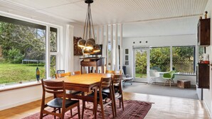 A spacious dining area with a wooden table and chairs, a hanging light fixture, and large windows offering a view of the outdoors. - Large summer house in Bandholm on Lolland (Bandholm)