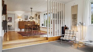 A modern living room with a dining area, a sofa, a lamp, and a view of the outdoors. - Large summer house in Bandholm on Lolland (Bandholm)