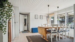 Un comedor con mesa de madera y sillas blancas, un tapete estampado y vistas amplias a través de ventanas grandes.