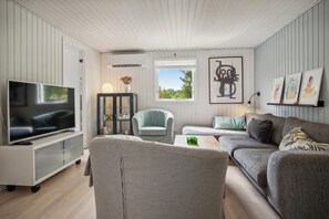 A modern living room with a flat-screen TV, a grey sofa, a light blue armchair, and a small table with a green object.