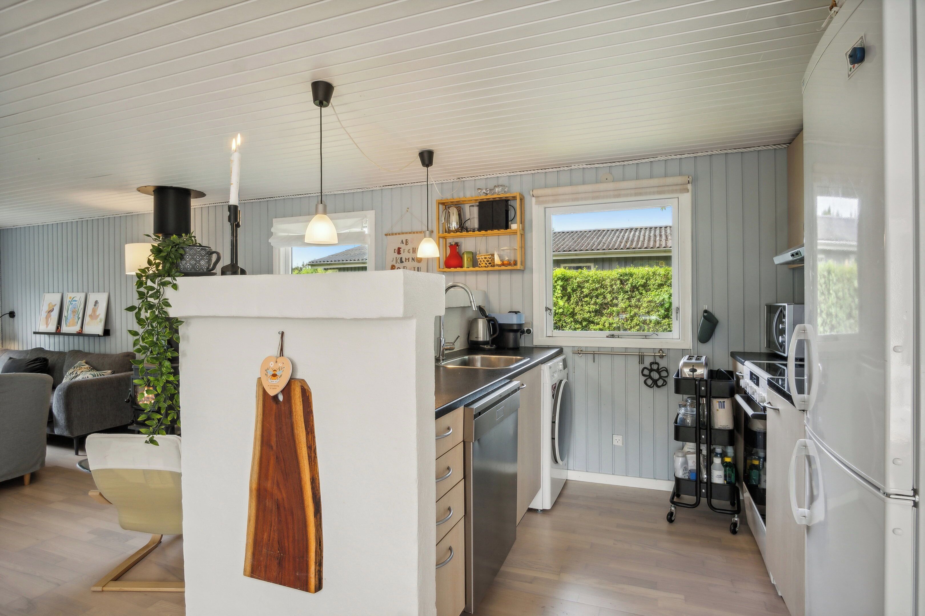 Una cocina moderna con lavavajillas, estufa y refrigerador. Se ve un ventanal con vista a la vegetación.