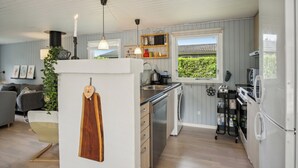 Una cocina moderna con lavavajillas, estufa y refrigerador. Se ve un ventanal con vista a la vegetación.