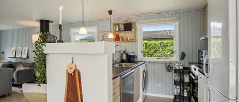 Una cocina moderna con lavavajillas, estufa y refrigerador. Se ve un ventanal con vista a la vegetación.
