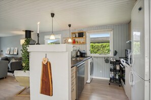 A modern kitchen with a dishwasher, stove, and refrigerator. There is a window with a view of greenery outside. - Lovely cottage in Pøt Strandby (Juelsminde)