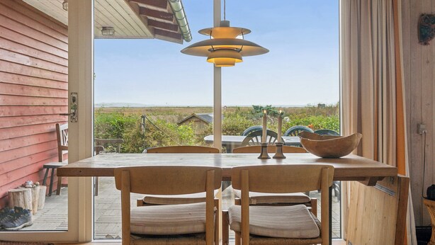 Un área de comedor con mesa y sillas, una lámpara colgante y vistas a través de un vidrio.