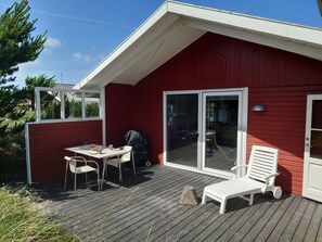 A red building with a covered patio, a table with chairs, and a grill. - Lovely summer house on natural grounds (Frøstrup)