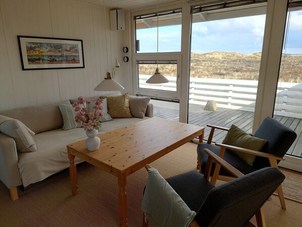 A room with a wooden table, a sofa, and a chair. There is a window with a view of the outdoors.