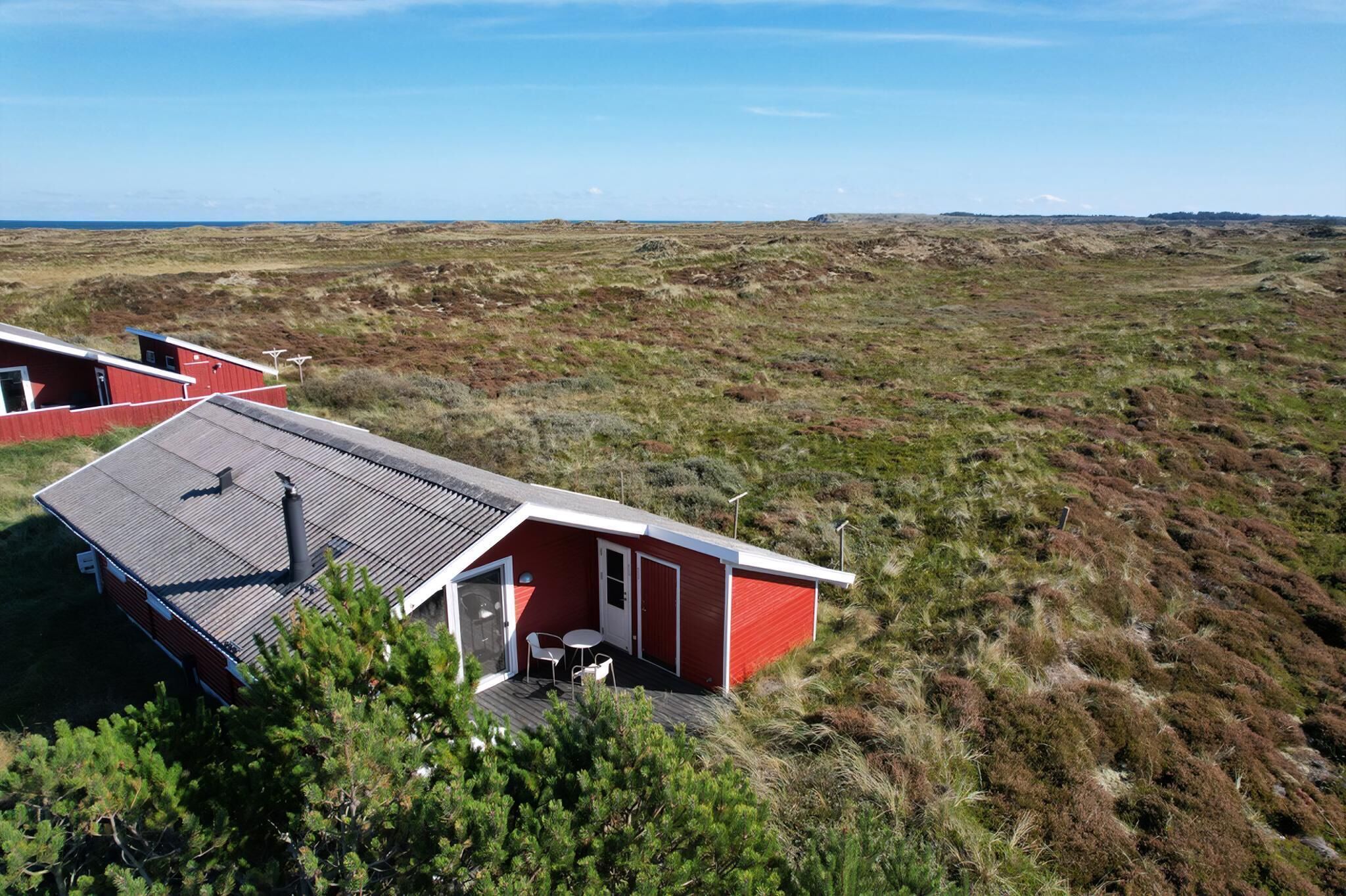 Un edificio rojo con techo plano, un pequeño patio con mesa y sillas, y vista a un paisaje árido.