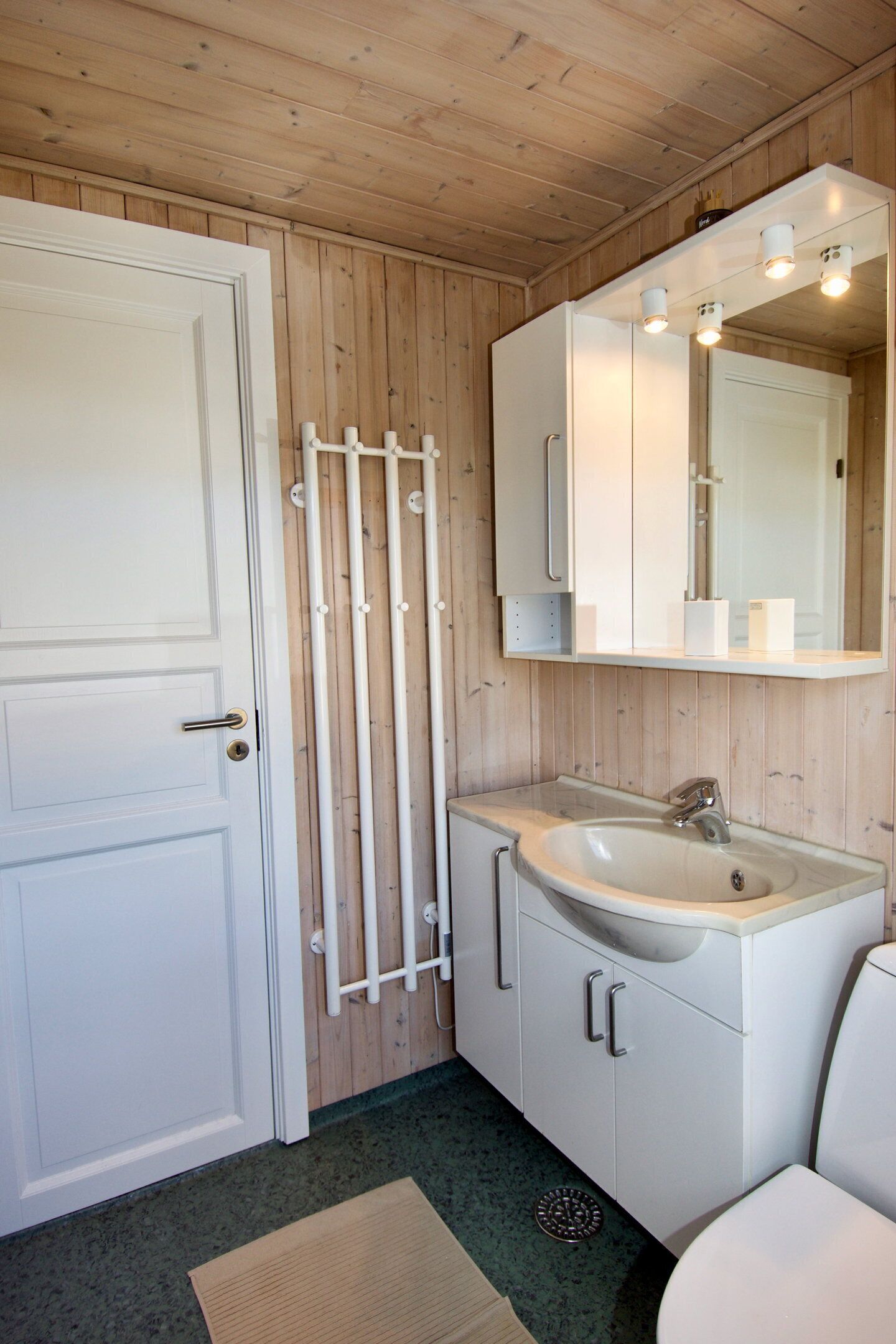 A bathroom with a white door, a sink, a mirror, and a towel rack.