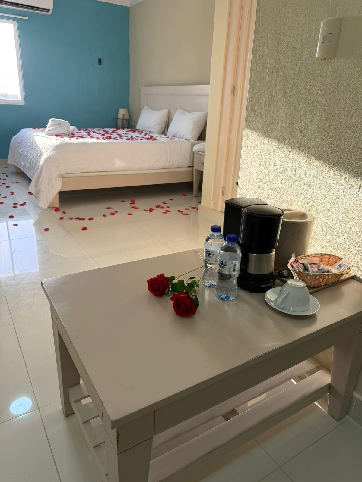 Een hotelkamer met een bed, een tafel met waterflesjes, een koffiezetapparaat en een mand.