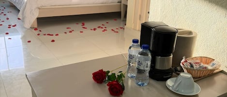 Een hotelkamer met een bed, een tafel met waterflesjes, een koffiezetapparaat en een mand.