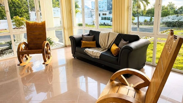 A spacious room with a large window, a black sofa, wooden rocking chairs, and a tiled floor. - Hotel El Imperio Punta Cana (Punta Cana)