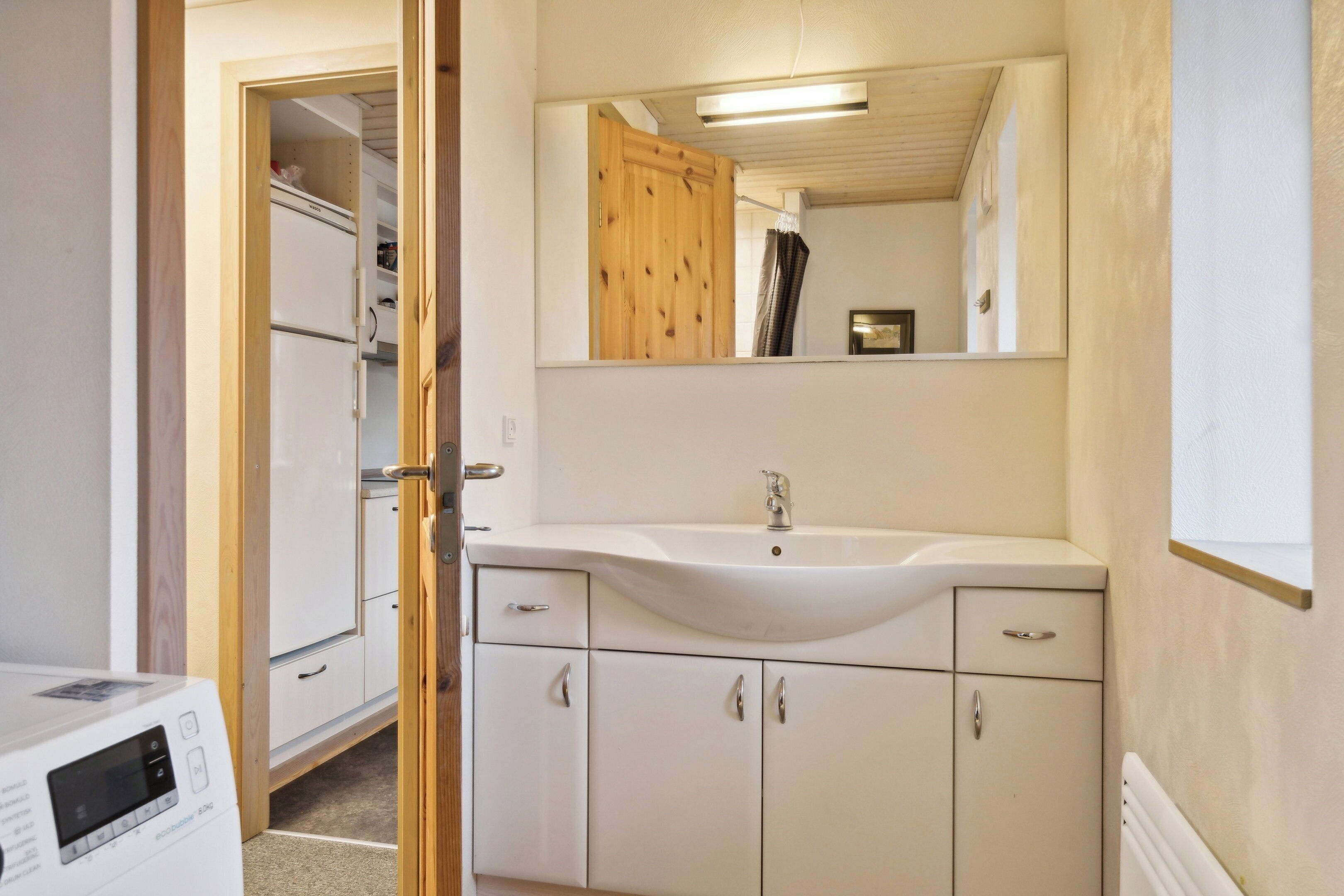 A compact bathroom with a white sink, mirror, and wooden door.