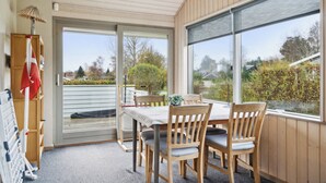 Een overdekt terras met een tafel en stoelen, een schuifpui en uitzicht op de omgeving.