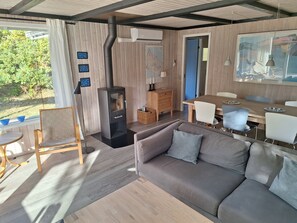 Ein modernes Wohnzimmer mit einer Couch, einem Esstisch mit Stühlen, einem Kamin und Blick ins Grüne.