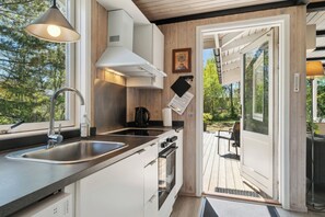 Eine moderne Küche mit Spüle aus Edelstahl, einem Einbauofen und einem durch die offene Tür einsehbaren Holzboden.