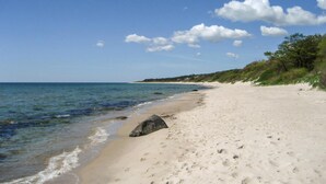 A sandy beach with clear blue water, a few rocks, and sparse vegetation along the shore. - Lovely family cottage near child-friendly beach (Aakirkeby)