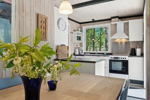 Una cocina moderna con armarios blancos, una mesa de madera y un jarrón azul con flores.