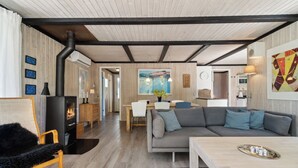 A modern living room with a fireplace, a sofa, a dining area, and a kitchen. - Lovely family cottage near child-friendly beach (Aakirkeby)