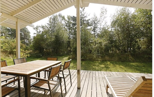 A covered outdoor area with a wooden table and chairs, surrounded by a lush green landscape.
