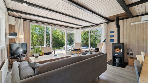A modern living room with a sofa, TV, and a wood-burning stove. - Lovely family cottage near child-friendly beach (Aakirkeby)