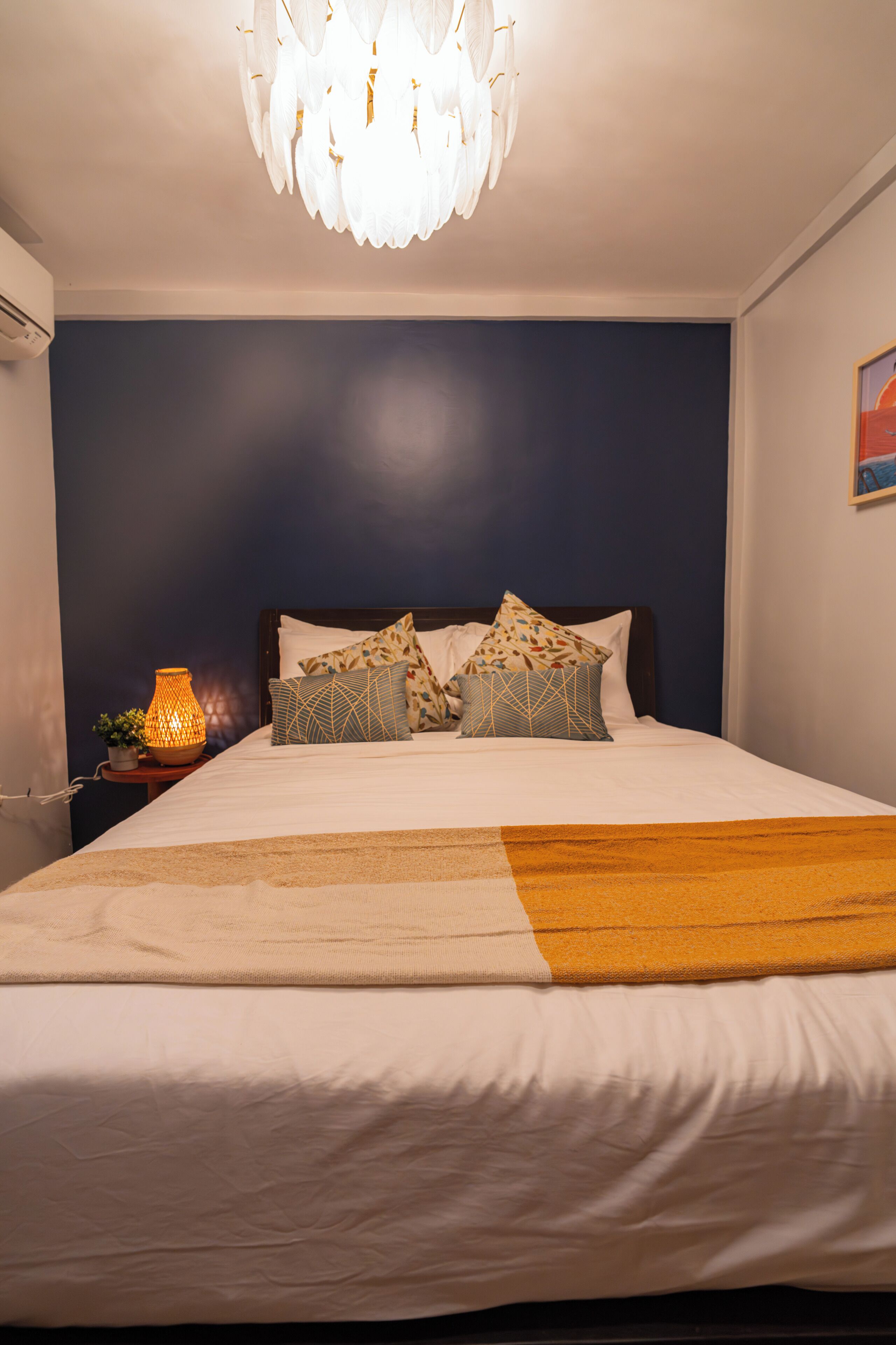 Una cama bien hecha con almohadones estampados, una lámpara de noche y un candelabro decorativo.