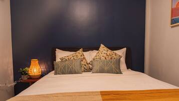 Una cama bien hecha con almohadones estampados, una lámpara de noche y un candelabro decorativo.