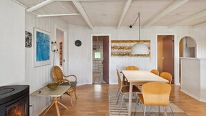 Een kamer met een open haard, een eettafel, stoelen en een keuken die door een open deur zichtbaar is.
