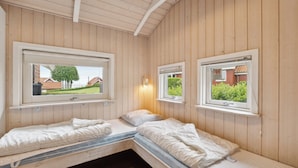 Een kamer met twee bedden, houten wanden en ramen met uitzicht op groen.