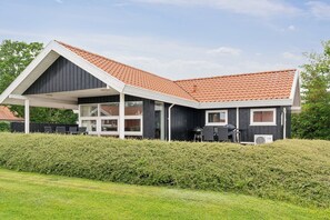 A modern house with a sloped roof, large windows, and a covered patio area. - Lovely summer house with sea view (Haderslev)