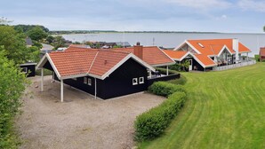 Een modern gebouw met een rode pannendak, een overdekt terras en uitzicht op een meer.