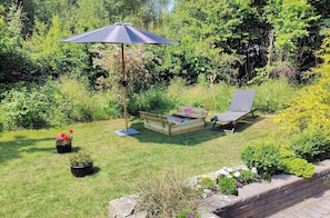 Un jardin avec un banc en bois, une chaise et un parasol.