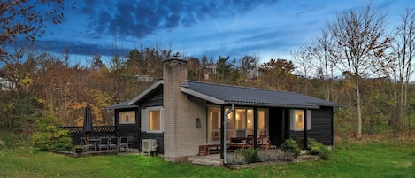 Ein eingeschossiges Haus mit einer Veranda, einem Schornstein und einem Rasen.