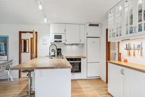 A modern kitchen with white cabinetry, a wooden countertop island, and a built-in oven. - Cozy cottage steps from Lyngsbæk beach (Ebeltoft)