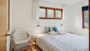 A bedroom with a bed, a chair, a window, and a lamp. - Cozy cottage steps from Lyngsbæk beach (Ebeltoft)