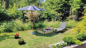 A garden with a wooden bench, a chair, and an umbrella. - Cozy cottage steps from Lyngsbæk beach (Ebeltoft)