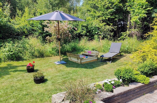 A garden with a wooden bench, a chair, and an umbrella.