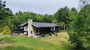 A house with a chimney, a covered porch, and a lawn. - Cozy cottage steps from Lyngsbæk beach (Ebeltoft)