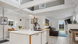 Eine moderne Küche mit einer zentralen Kochinsel, ein Essbereich mit Stühlen, eine Couch und eine Treppe, die in ein Obergeschoss führt.